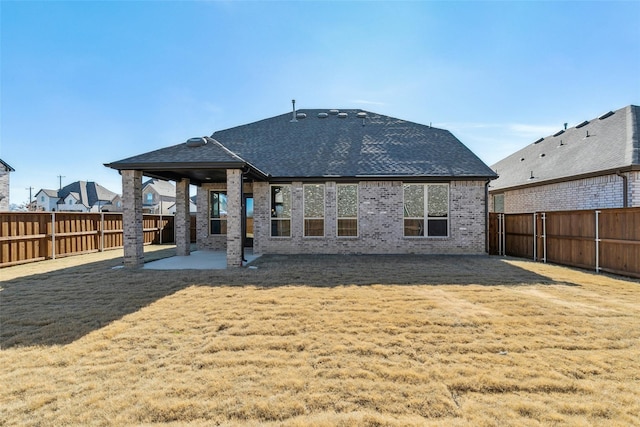 rear view of property with brick siding, a patio, a fenced backyard, and roof with shingles