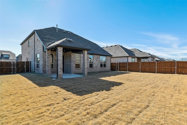 rear view of house with a shingled roof, brick siding, a fenced backyard, a patio area, and a yard