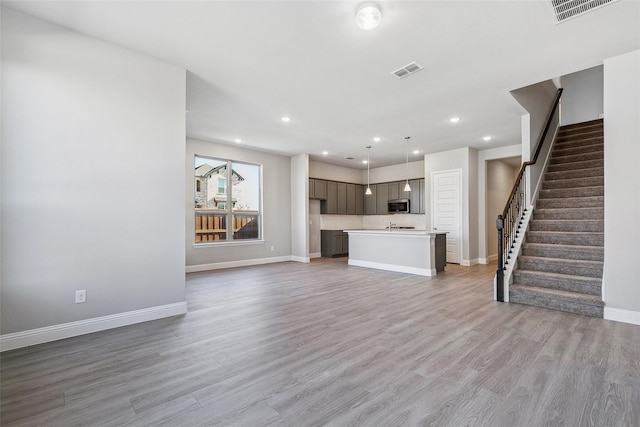 unfurnished living room featuring stairway, baseboards, light wood finished floors, and visible vents