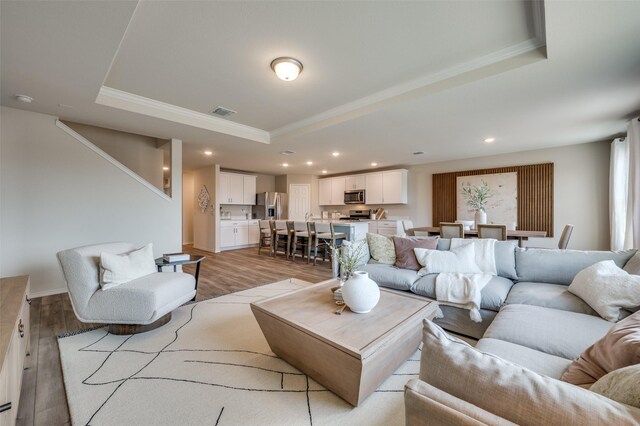 living area with crown molding, visible vents, recessed lighting, light wood-type flooring, and a raised ceiling