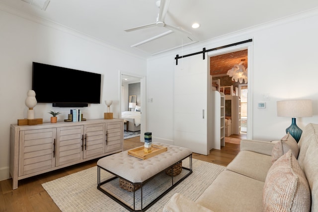 living room with ornamental molding, a ceiling fan, light wood finished floors, and a barn door