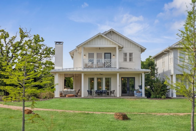 back of property featuring board and batten siding, a balcony, french doors, a ceiling fan, and a yard