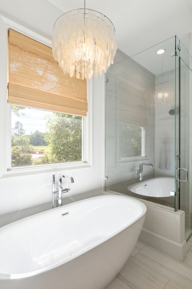 bathroom featuring a healthy amount of sunlight, a soaking tub, a shower stall, and a chandelier