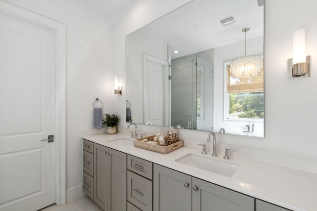 bathroom with double vanity, a notable chandelier, a shower stall, and a sink