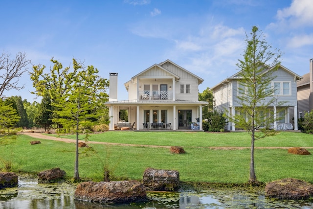 rear view of property featuring french doors, ceiling fan, a yard, and a balcony