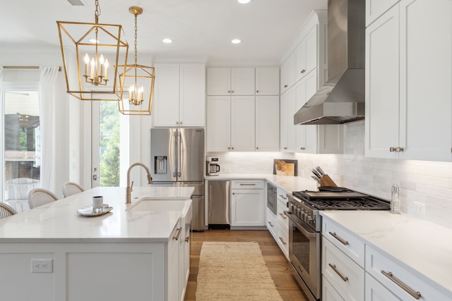kitchen with wall chimney range hood, appliances with stainless steel finishes, a notable chandelier, and a healthy amount of sunlight