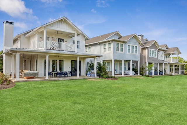 back of property featuring ceiling fan, an outdoor living space, a chimney, a balcony, and a yard