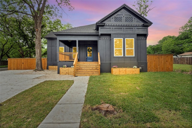 bungalow with roof with shingles, fence, a front lawn, board and batten siding, and a porch