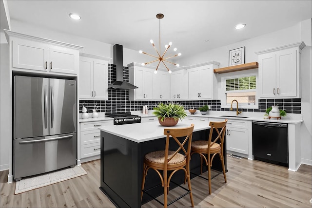 kitchen with wall chimney range hood, dishwasher, a sink, freestanding refrigerator, and light wood-style flooring