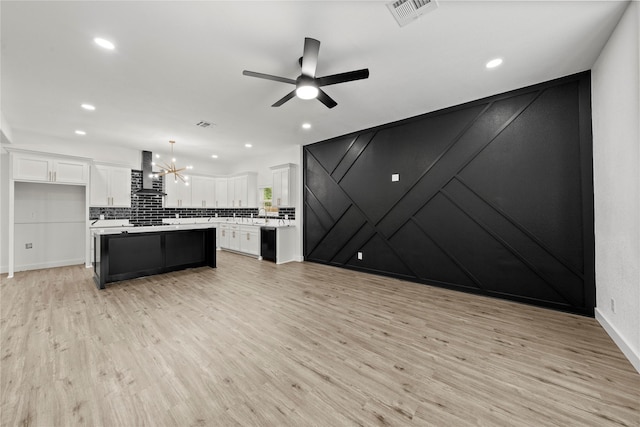 kitchen featuring white cabinets, wall chimney exhaust hood, a center island, ceiling fan with notable chandelier, and visible vents