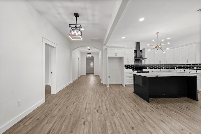 kitchen featuring an inviting chandelier, decorative backsplash, light countertops, wall chimney exhaust hood, and arched walkways