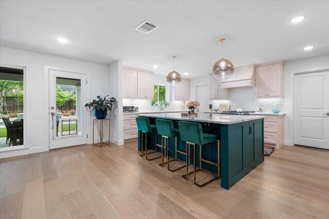 kitchen featuring visible vents, custom exhaust hood, a kitchen island, light wood-style floors, and light countertops
