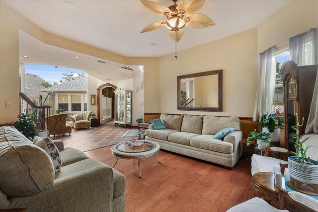 living area with arched walkways, a ceiling fan, and wood finished floors