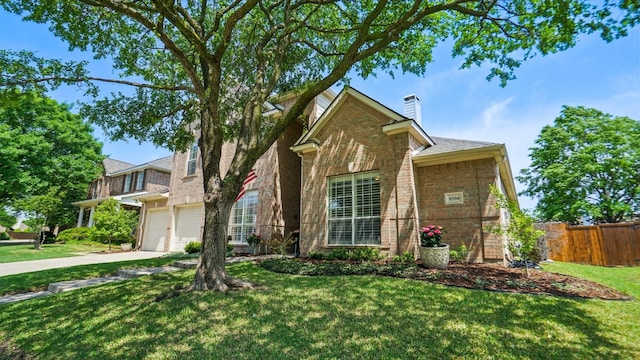 traditional home with fence, an attached garage, brick siding, a chimney, and driveway