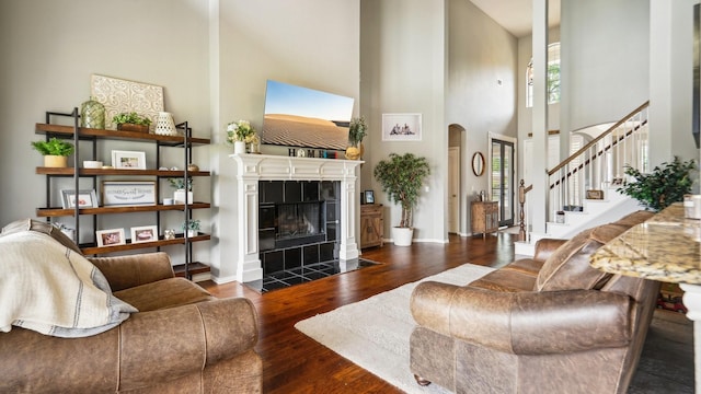 living area with a high ceiling, arched walkways, a tiled fireplace, stairs, and wood finished floors