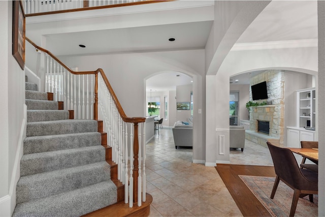 entrance foyer featuring arched walkways, a stone fireplace, ornamental molding, and stairway