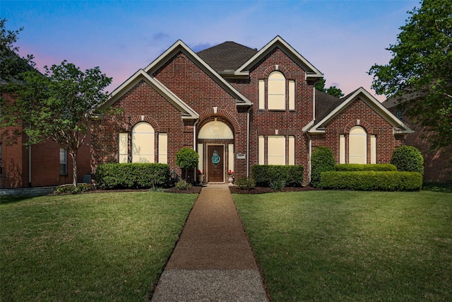 traditional home featuring brick siding, a shingled roof, and a front yard