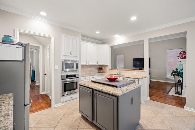 kitchen with white cabinets, appliances with stainless steel finishes, light tile patterned floors, a kitchen island, and ornamental molding