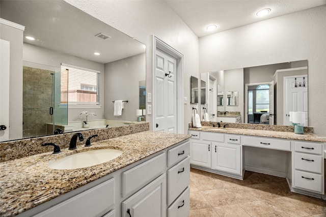 full bath with visible vents, a sink, two vanities, and a shower stall