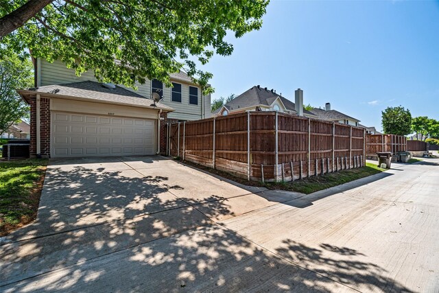 view of property exterior with fence, brick siding, a garage, central AC unit, and driveway