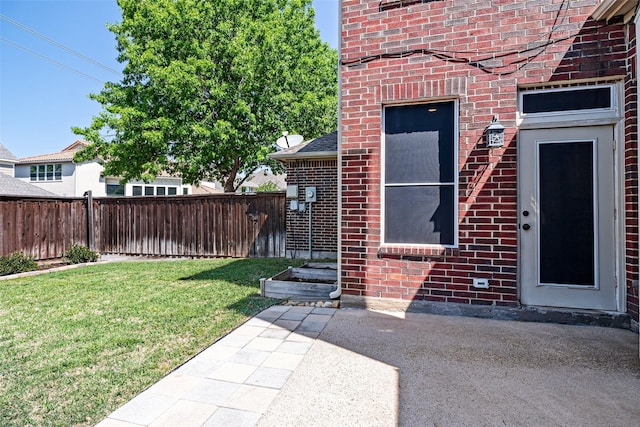 entrance to property featuring brick siding, a lawn, fence, and a patio area
