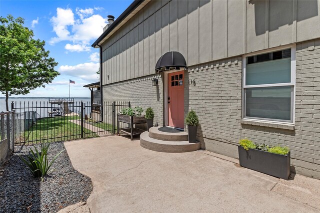 view of exterior entry featuring brick siding, a water view, fence, and a patio area