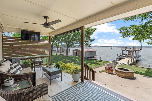 view of patio featuring a ceiling fan, a boat dock, boat lift, an outdoor living space with a fire pit, and a water view