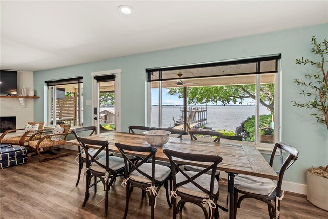 dining room with a brick fireplace, wood finished floors, baseboards, a water view, and recessed lighting