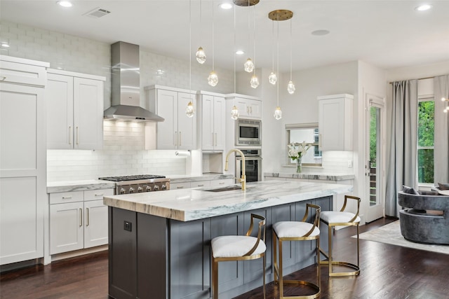 kitchen with wall chimney range hood, backsplash, visible vents, a sink, and stainless steel appliances