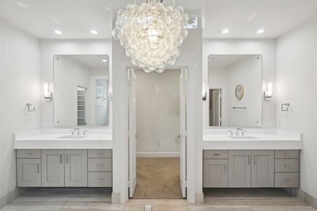 bathroom with a chandelier, two vanities, a sink, and wood finished floors