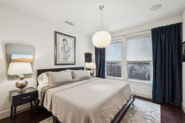bedroom with baseboards, visible vents, and wood finished floors