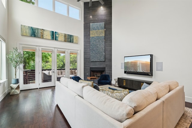 living room featuring wood finished floors, baseboards, a high ceiling, a large fireplace, and french doors