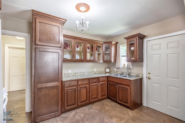 kitchen with an inviting chandelier, pendant lighting, brown cabinetry, light stone countertops, and a sink
