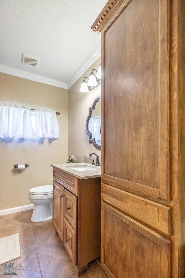 half bathroom featuring visible vents, vanity, baseboards, toilet, and ornamental molding