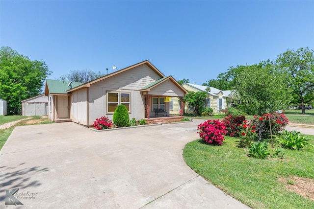 ranch-style home featuring covered porch, a front yard, an outbuilding, a shed, and concrete driveway