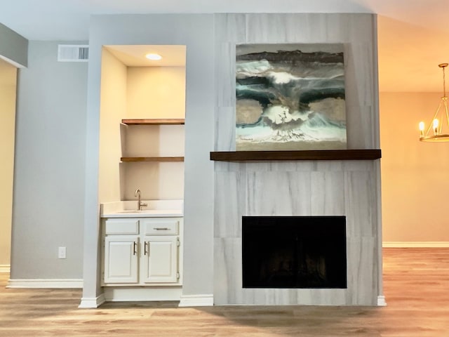 interior space with a fireplace, a sink, baseboards, light wood finished floors, and an inviting chandelier