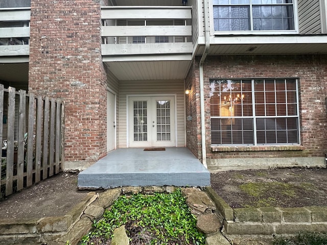 doorway to property featuring brick siding, fence, and french doors