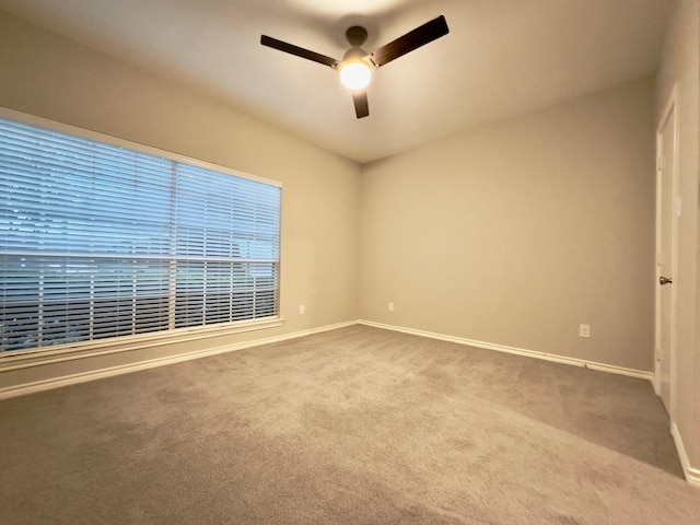 carpeted spare room featuring baseboards and a ceiling fan
