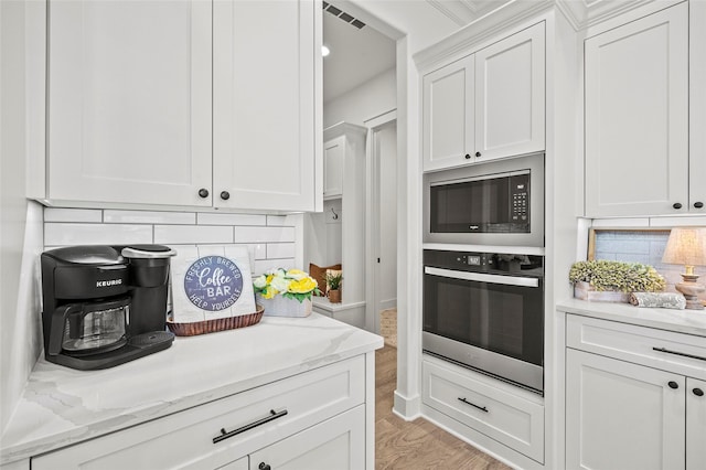4771 Sasha Way, Caddo Mills, TX 75135 - kitchen with visible vents, stainless steel oven, built in microwave, white cabinets, and light wood finished floors