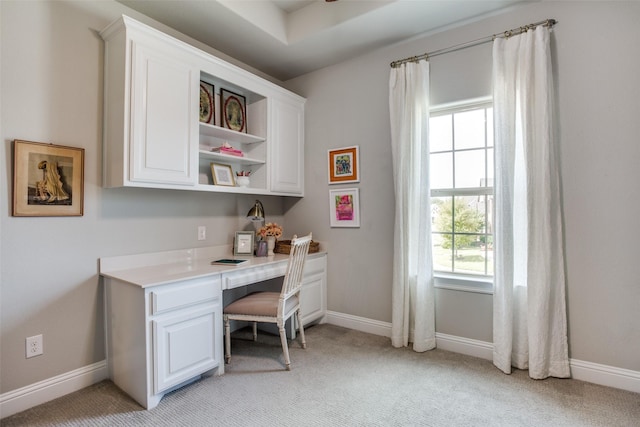office area featuring baseboards, built in desk, and light carpet