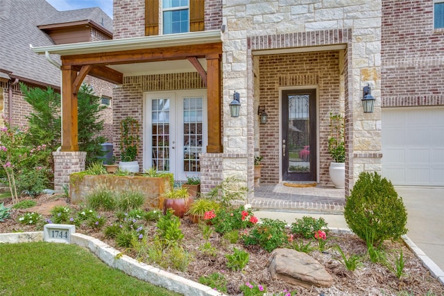 entrance to property featuring a garage, covered porch, stone siding, french doors, and brick siding