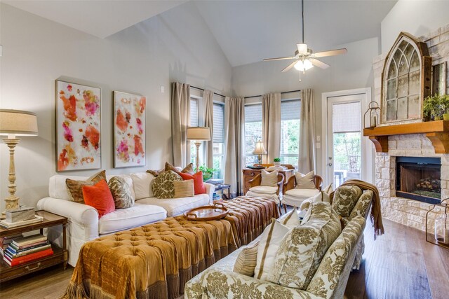 living area with ceiling fan, a stone fireplace, wood finished floors, and lofted ceiling