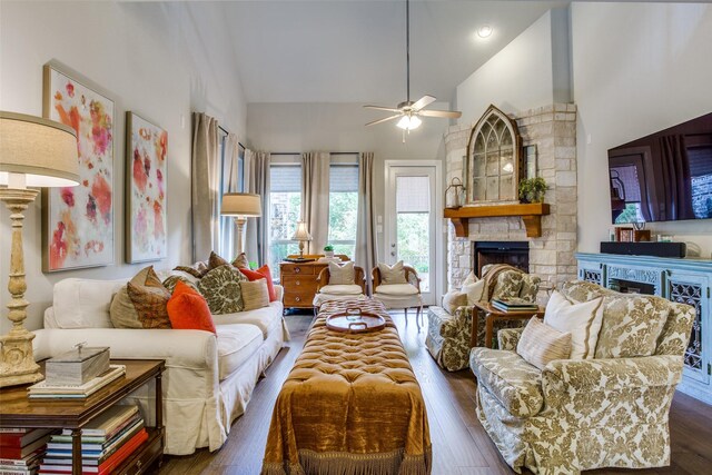 living area featuring a stone fireplace, ceiling fan, wood finished floors, and high vaulted ceiling