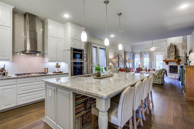 kitchen with tasteful backsplash, stainless steel gas cooktop, a fireplace, a sink, and wall chimney exhaust hood