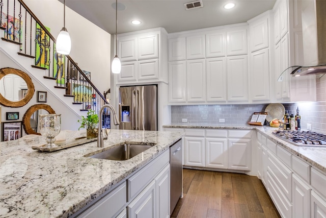 kitchen with appliances with stainless steel finishes, a sink, wall chimney exhaust hood, visible vents, and hardwood / wood-style flooring