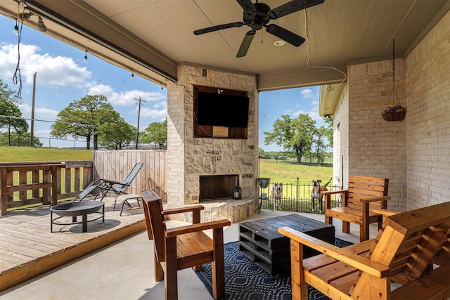view of patio / terrace featuring an outdoor stone fireplace, fence, and a ceiling fan