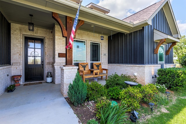 view of exterior entry with brick siding, board and batten siding, roof with shingles, and covered porch