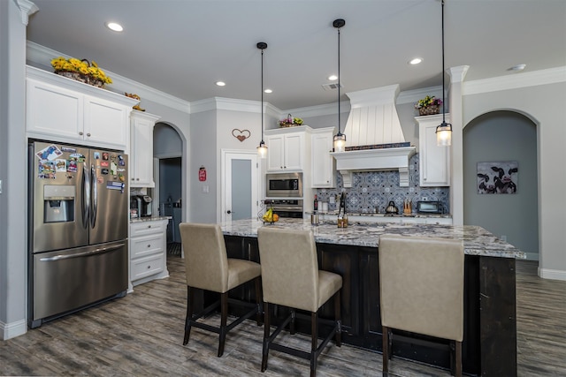 kitchen with arched walkways, stainless steel appliances, white cabinetry, custom range hood, and tasteful backsplash