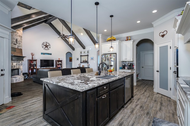kitchen featuring arched walkways, appliances with stainless steel finishes, a fireplace, a sink, and white cabinets