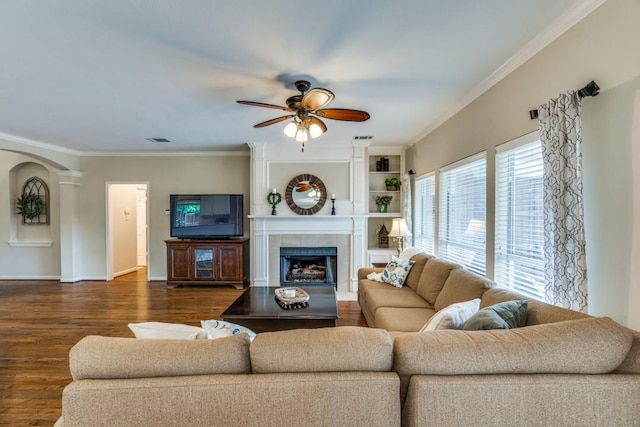 living area featuring ceiling fan, arched walkways, dark wood finished floors, a tiled fireplace, and visible vents